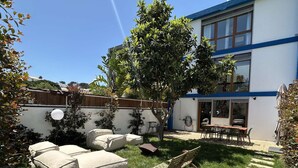 Ein Garten mit Sitzgelegenheiten im Freien, einem Baum und einem Gebäude mit großen Fenstern.