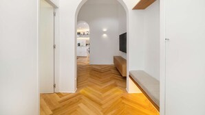 A hallway with a herringbone floor leading to a kitchen area with white cabinets and a microwave.