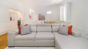 A modern living room with a grey sectional sofa, a dining area with a round table, and a kitchen area with white cabinetry. - Timeless Design Meets Central Convenience (Lisbon)
