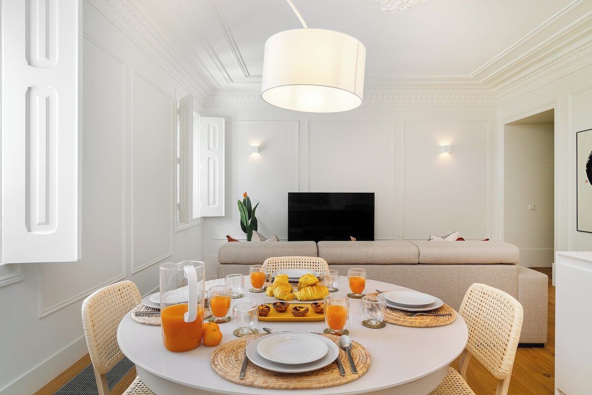 A dining area with a round table set for breakfast, a sofa in the background, and a television on the wall.