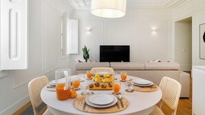 A dining area with a round table set for breakfast, a sofa in the background, and a television on the wall. - Timeless Design Meets Central Convenience (Lisbon)