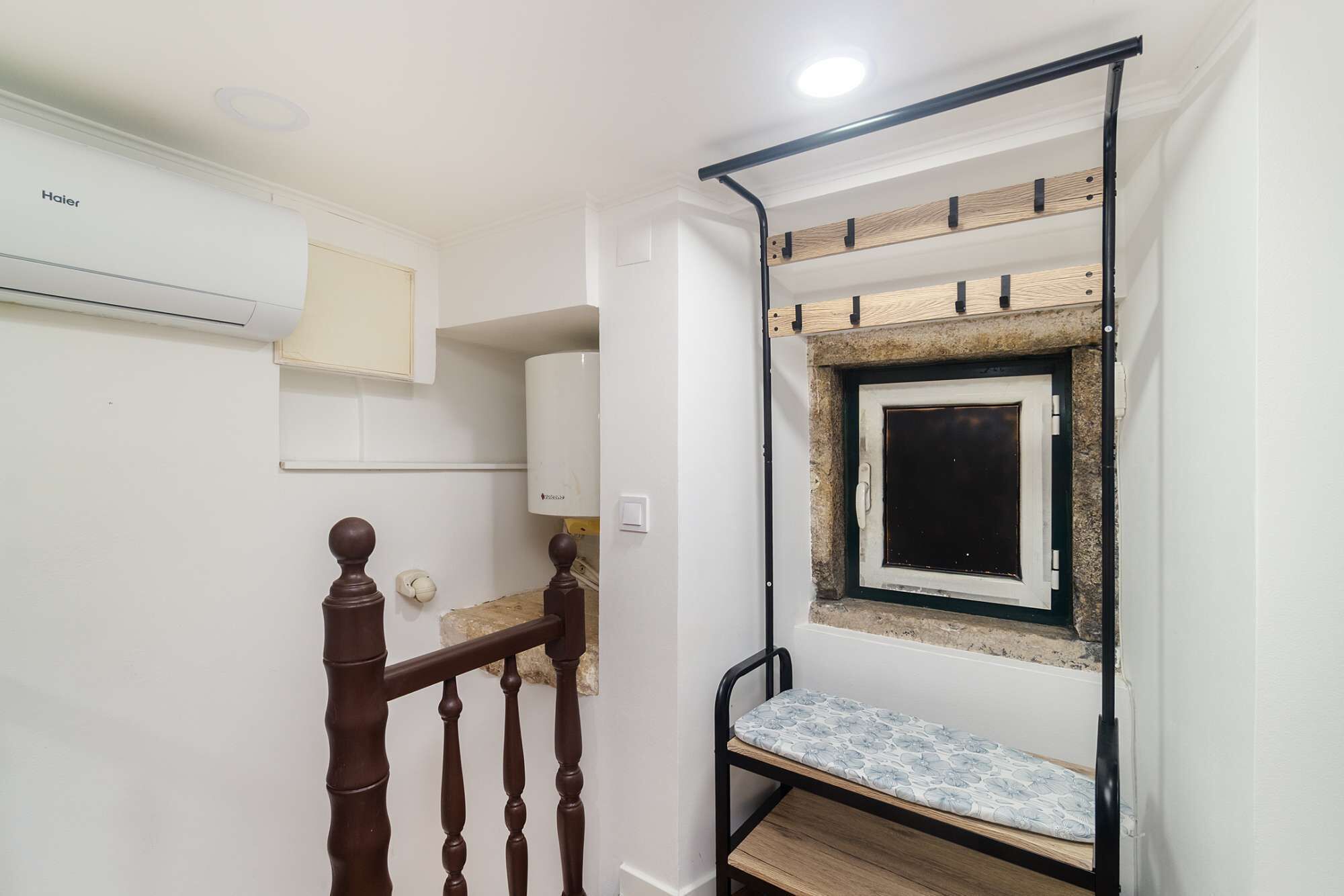 Una habitación pequeña con un banco de madera, una ventana enmarcada en piedra y una pared blanca con un aire acondicionado instalado.