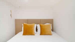 Een eenpersoonsbed met een beige hoofdbord en twee geel-mosterdkleurige kussens.