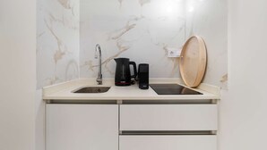Eine kleine Küchenzeile mit Spüle, einer Bosch-Kaffeemaschine, einem Krups-Wasserkocher und einem Holztablett.
