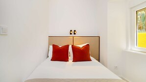 Ein Schlafzimmer mit einem Bett, zwei Nachttischlampen, einem Fenster und einem an der Wand befestigten Lichtschalter.