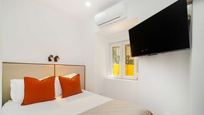 Ein Hotelzimmer mit Bett, Klimaanlage, einem an der Wand befestigten Fernseher und einem Fenster mit gelben Jalousien.