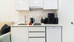 Una kitchenette compacta con un lavamanos, una cafetera, un microondas y un refrigerador pequeño.