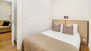 Un dormitorio con cama, dos lámparas de noche y una puerta que da a otra habitación.