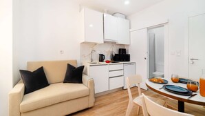 Un espacio habitable compacto con kitchenette, un sofá, una mesa de comedor con sillas y una puerta que da a un baño.