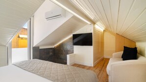 A bedroom with a sloped ceiling, a flat-screen TV mounted on the wall, a bed with a quilted cover, and a wooden floor. - Modern Comfort Meets Old Lisbon Charm (Lisbon)