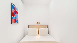 Une chambre à coucher au style minimaliste, avec un lit, deux lampes fixées au mur et un tableau abstrait aux couleurs vives.