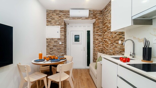 Une cuisine compacte avec un coin repas, un four encastré et une porte blanche.