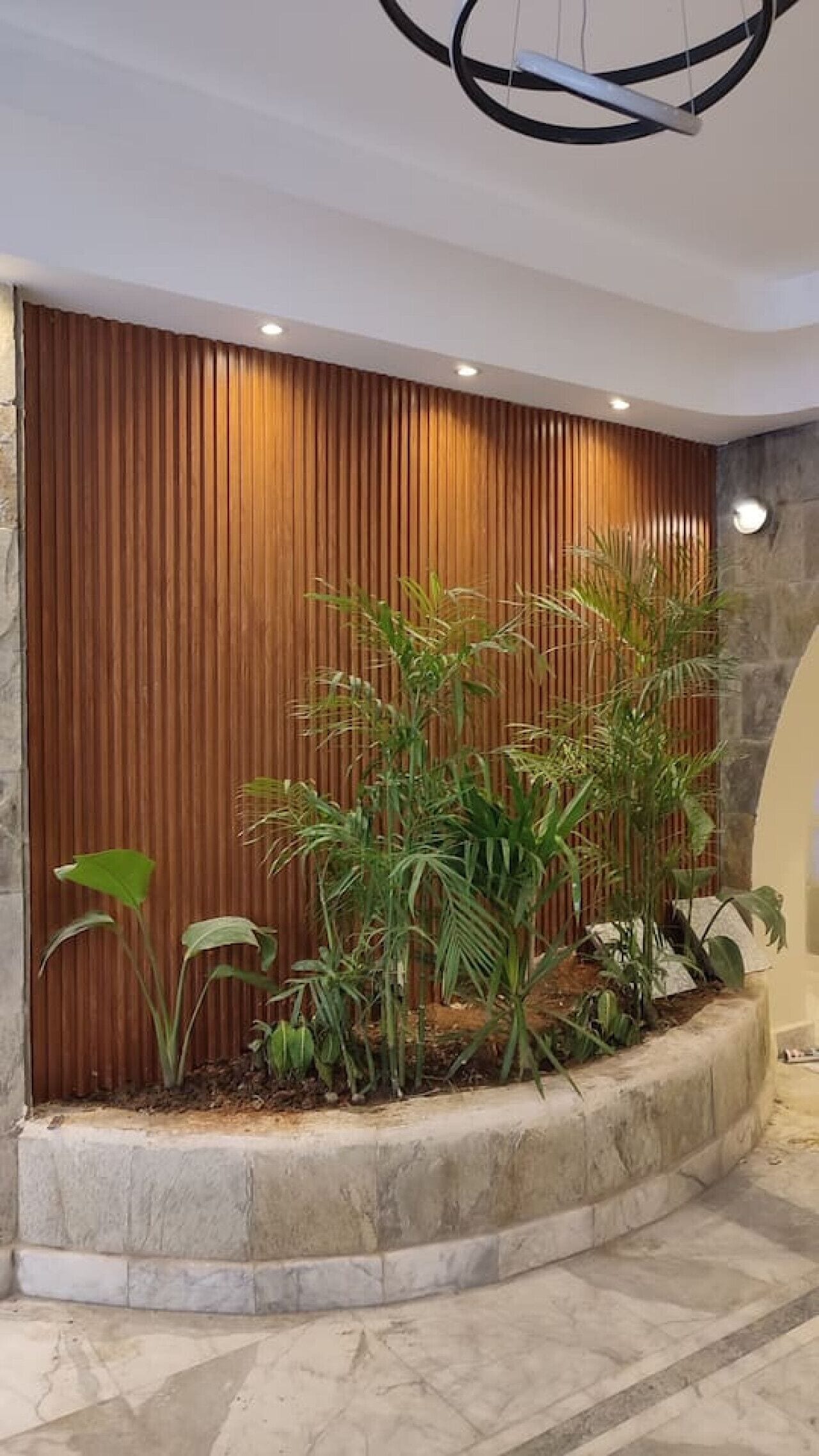 Ein modernes Interieur mit einer Holzwand, einem Betongartentopf mit tropischen Pflanzen und einer Steinwand.