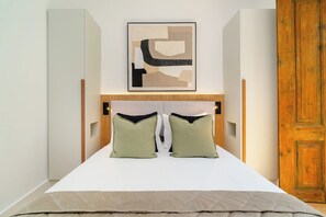 A neatly made bed with a white mattress, two green pillows, and a beige throw blanket.