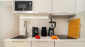 Una cocina compacta con microondas, cafetera, licuadora y tabla de cortar de madera.