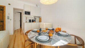 Une cuisine moderne avec des meubles blancs, un four à micro-ondes et une machine à café. On y trouve une table à manger mise avec des assiettes, des verres et du jus d’orange.