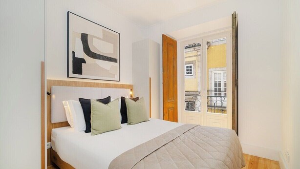 Une chambre à coucher avec un lit, une tête de lit en bois, une grande fenêtre et une porte donnant sur un balcon.