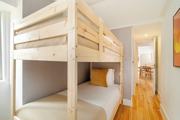 A bunk bed with a grey headboard and a lower bed with a white mattress and a brown pillow.