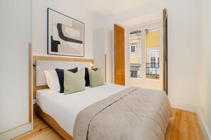 Ein Schlafzimmer mit Bett, Kissen, einem Kopfteil, einer Tür und einem Fenster mit Blick auf Gebäude.