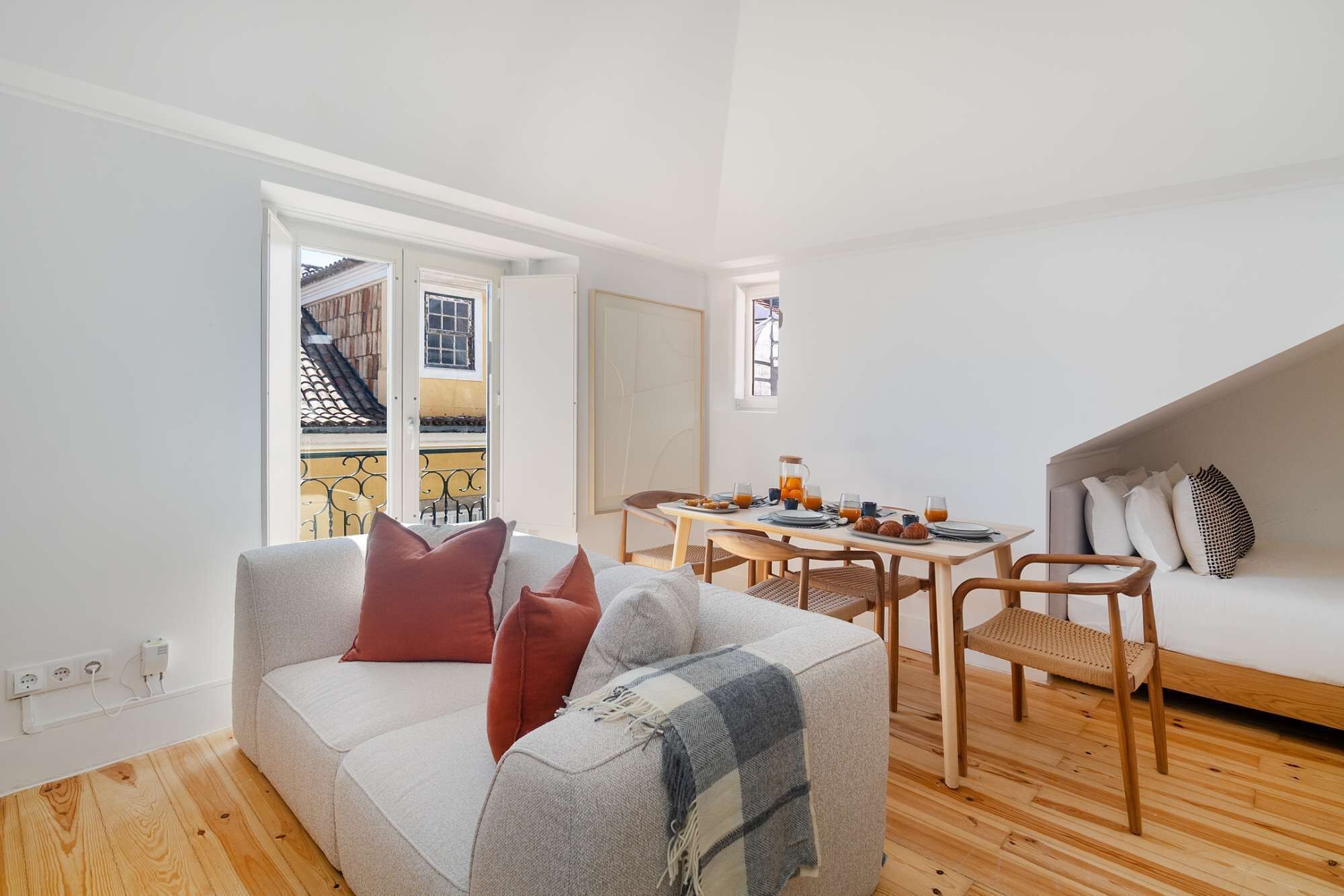 Uma sala de estar moderna com sofá, mesa de jantar e cadeiras, e vista para o exterior.