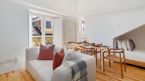A modern living room with a sofa, a dining table with chairs, and a view of the outside. - Live Like a Local in Vibrant Bairro Alto (Lisboa)