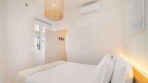 Ein Schlafzimmer mit einem Bett, weißen Wänden, einer Klimaanlage und einer Tür zu einem anderen Raum.