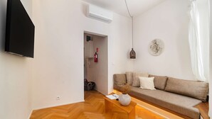 A modern living room with a sofa, a wooden floor, a flat-screen TV, and a wall-mounted air conditioner. - Lisbon Charm: Walk to Graça Viewpoints (Lisbon)