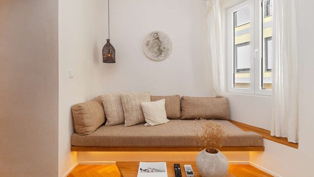 A modern living room with a beige sofa, a hanging light fixture, a decorative plate, and a vase with dried flowers on a wooden coffee table. - Lisbon Charm: Walk to Graça Viewpoints (Lisbon)