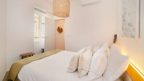 Een slaapkamer met een bed, nachtkastje, hanglamp en een wandairconditioner.