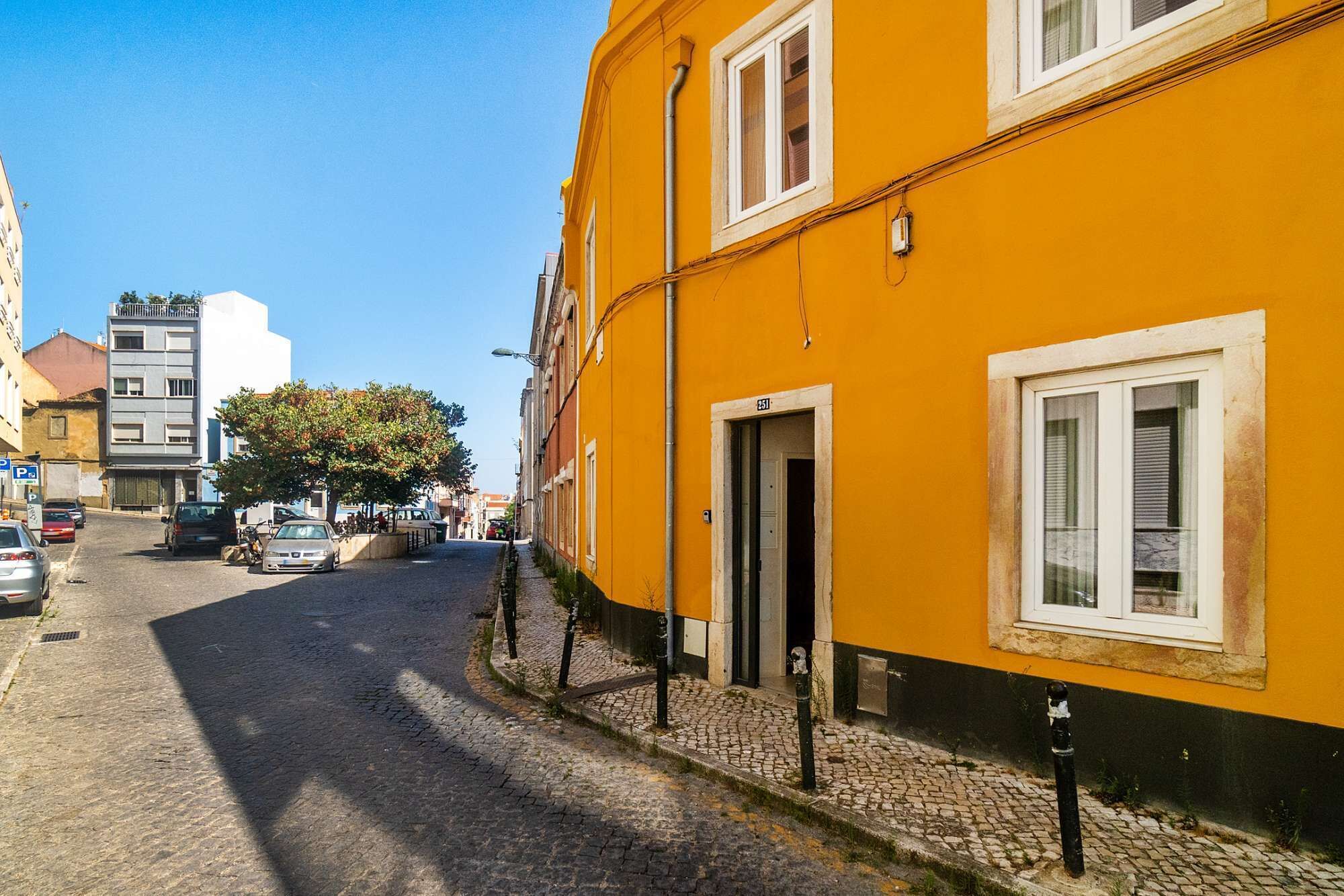 Une ruelle étroite pavée, bordée d’immeubles, dont un bâtiment jaune remarquable avec une porte et une fenêtre.