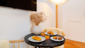 A cozy dining area with a round table set for breakfast, including croissants and orange juice, and a vase with dried flowers. - Lisbon Charm: Walk to Graça Viewpoints (Lisbon)