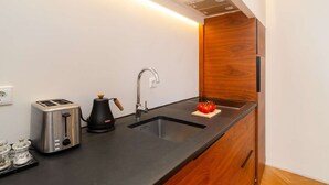 A compact kitchen with a black countertop, stainless steel toaster, coffee maker, and a wooden cabinet. - Lisbon Charm: Walk to Graça Viewpoints (Lisbon)