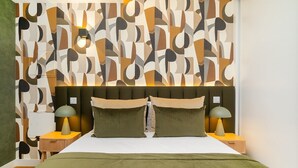 A modern bedroom with a geometric patterned wall, a large bed with green bedding, two bedside lamps, and a headboard with a light fixture. - Light-Filled Studio with a True Neighborhood Feel (Lisbon)