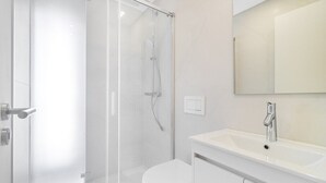 A modern bathroom with a glass shower enclosure, a white toilet, and a sink with a mirror above it. - Light-Filled Studio with a True Neighborhood Feel (Lisbon)