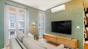 A living room with a sofa, a TV, a wooden console, and a balcony with a railing. - Light-Filled Studio with a True Neighborhood Feel (Lisbon)