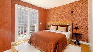 Ein Schlafzimmer mit einem großen Bett, einem Fenster mit Blick auf geparkte Autos und einer Wand mit Muster.