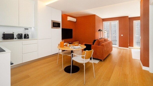 Eine moderne Küche mit weißen Schränken, ein Essbereich mit rundem Tisch und Stühlen sowie eine Wohnbereich mit Sofa und Fernseher.