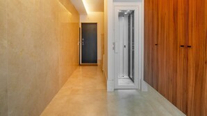 Un couloir avec une porte en bois, un ascenseur blanc et un sol en marbre.