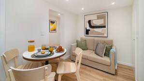 A modern living room with a round dining table, two chairs, a sofa, and abstract art on the wall. - Old Town Flat with a Modern Touch (Lisbon)