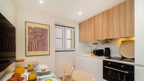 A modern kitchen with wooden cabinets, a black stove, and a dining area with breakfast items. - Old Town Flat with a Modern Touch (Lisbon)