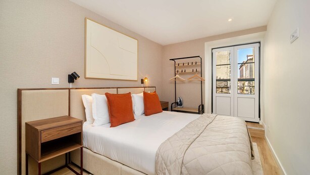 A bedroom with a bed, bedside table, and a wall-mounted ironing board. - Old Town Flat with a Modern Touch (Lisbon)