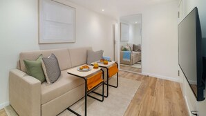 A modern living room with a sofa, a small table with breakfast items, a TV, and a mirror reflecting another room. - Old Town Flat with a Modern Touch (Lisbon)
