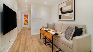 A modern living room with a flat-screen TV, a dining table with orange chairs, a beige sofa, and abstract art on the wall. - Old Town Flat with a Modern Touch (Lisbon)
