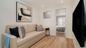 A modern living room with a beige sofa, patterned cushions, a framed abstract painting, a flat-screen TV, and a wooden floor. - Old Town Flat with a Modern Touch (Lisbon)