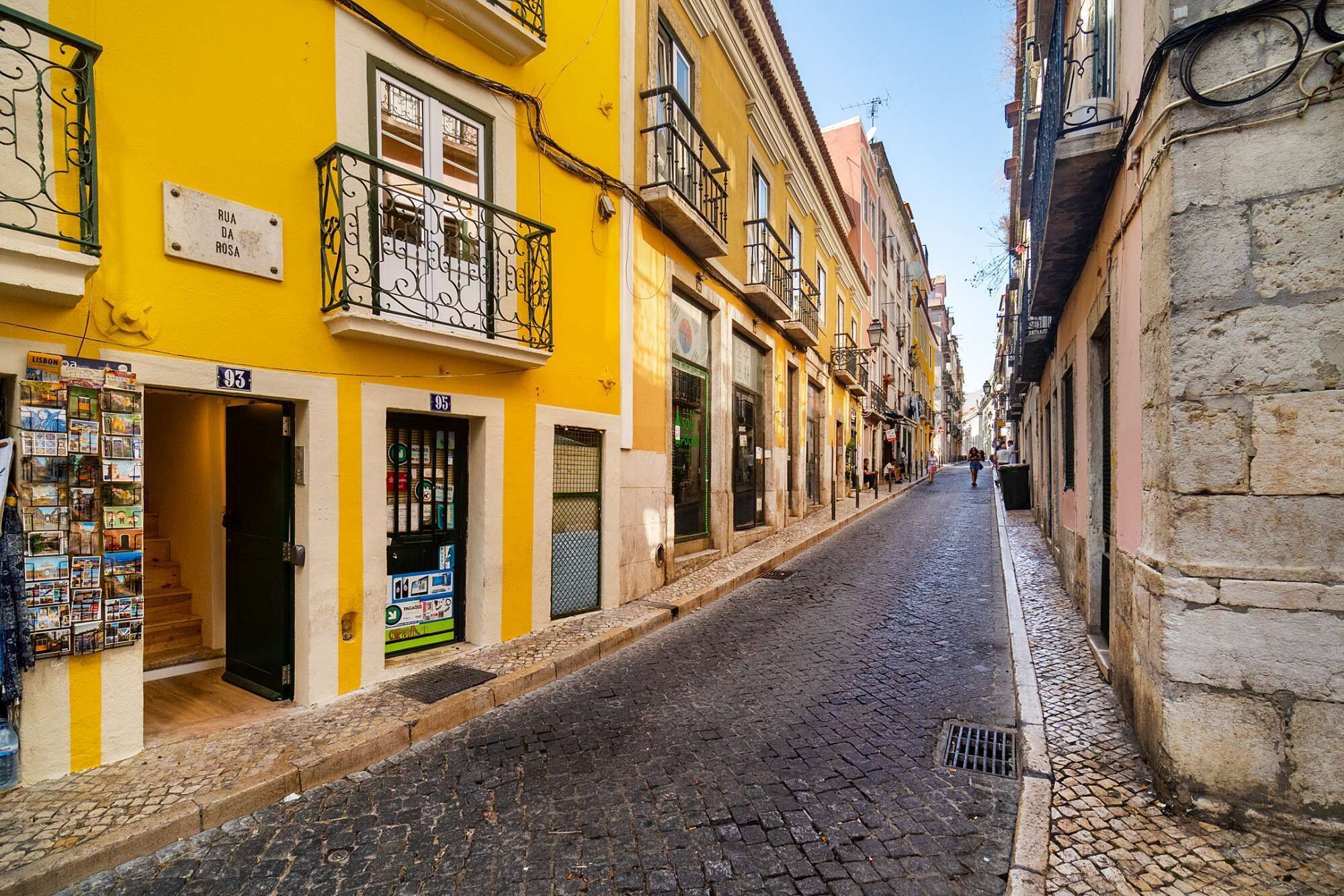 A narrow street lined with yellow buildings, some with balconies and signage.