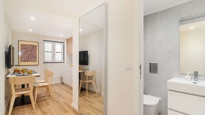 Ett modernt och väl upplyst rum med en matplats, en TV och ett badrum med en stor spegel och vita sanitetsporslin.