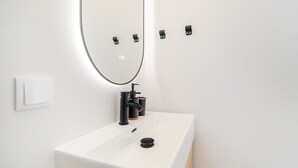 A white bathroom with a rectangular sink, a black faucet, and a mirror above it. - Sunny Studio Stay in Central Oeiras (Oeiras)