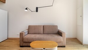 A modern living room with a brown sofa, a wooden coffee table, and a unique black wall-mounted lamp. - Sunny Studio Stay in Central Oeiras (Oeiras)