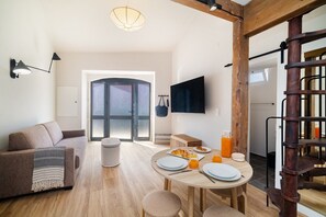 A spacious living area with a sofa, a dining table set with plates and a glass of orange juice, and a television mounted on the wall.