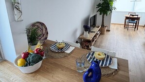 Zona de menjador amb taula de fusta preparada per a dues persones, amb sobretaules de ratlles i un bol de fruita.